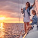 two happy female friends have fun relaxing yacht with glasses wine hands during sunset high seas